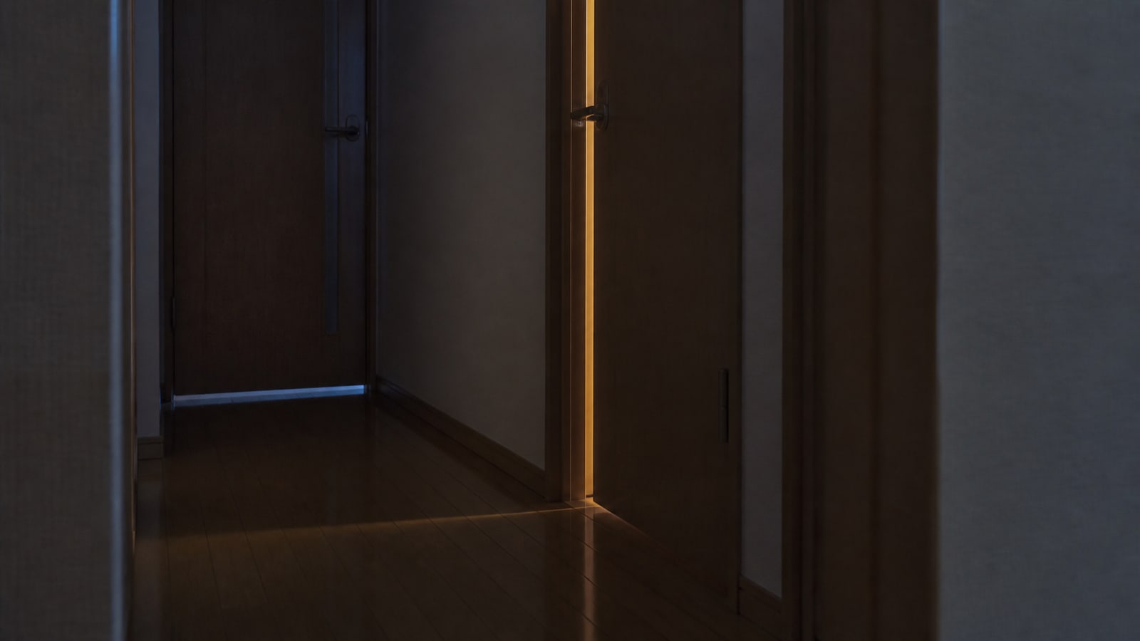 夜の廊下で、少しだけ開いた扉から暖かな光が漏れている様子